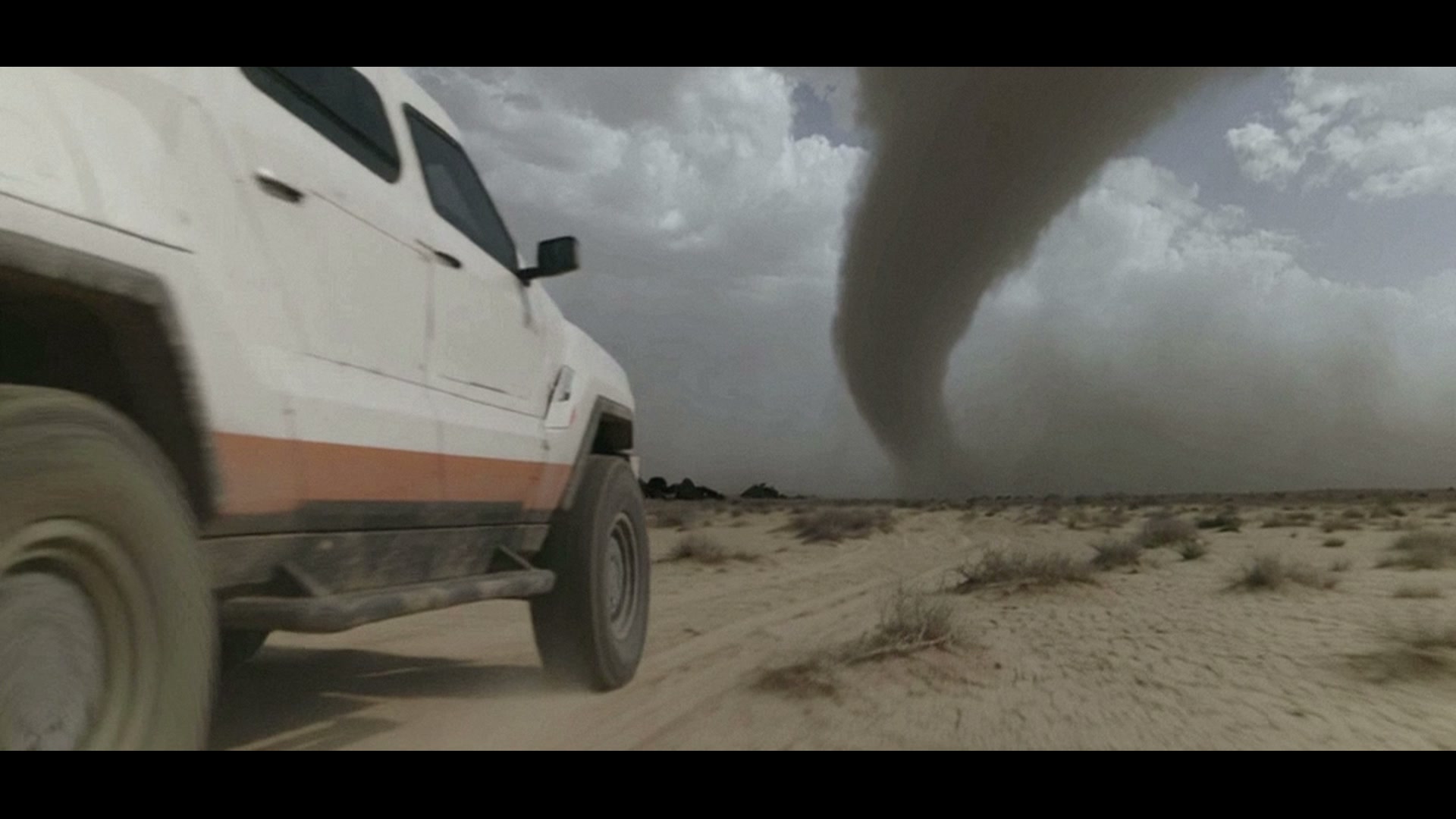 A white storm vehicle approaches a tornado across the desert