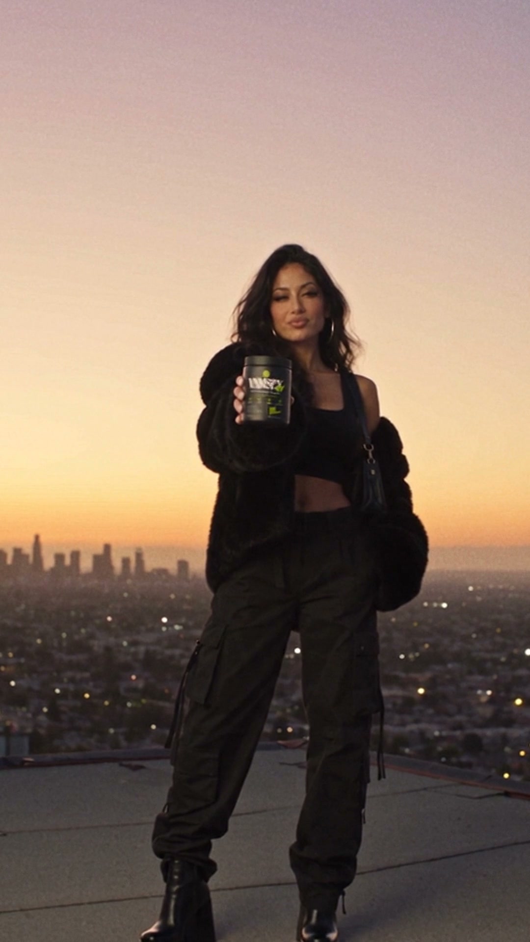Woman holding the VNMSFX greens product on a rooftop above the city at sunset